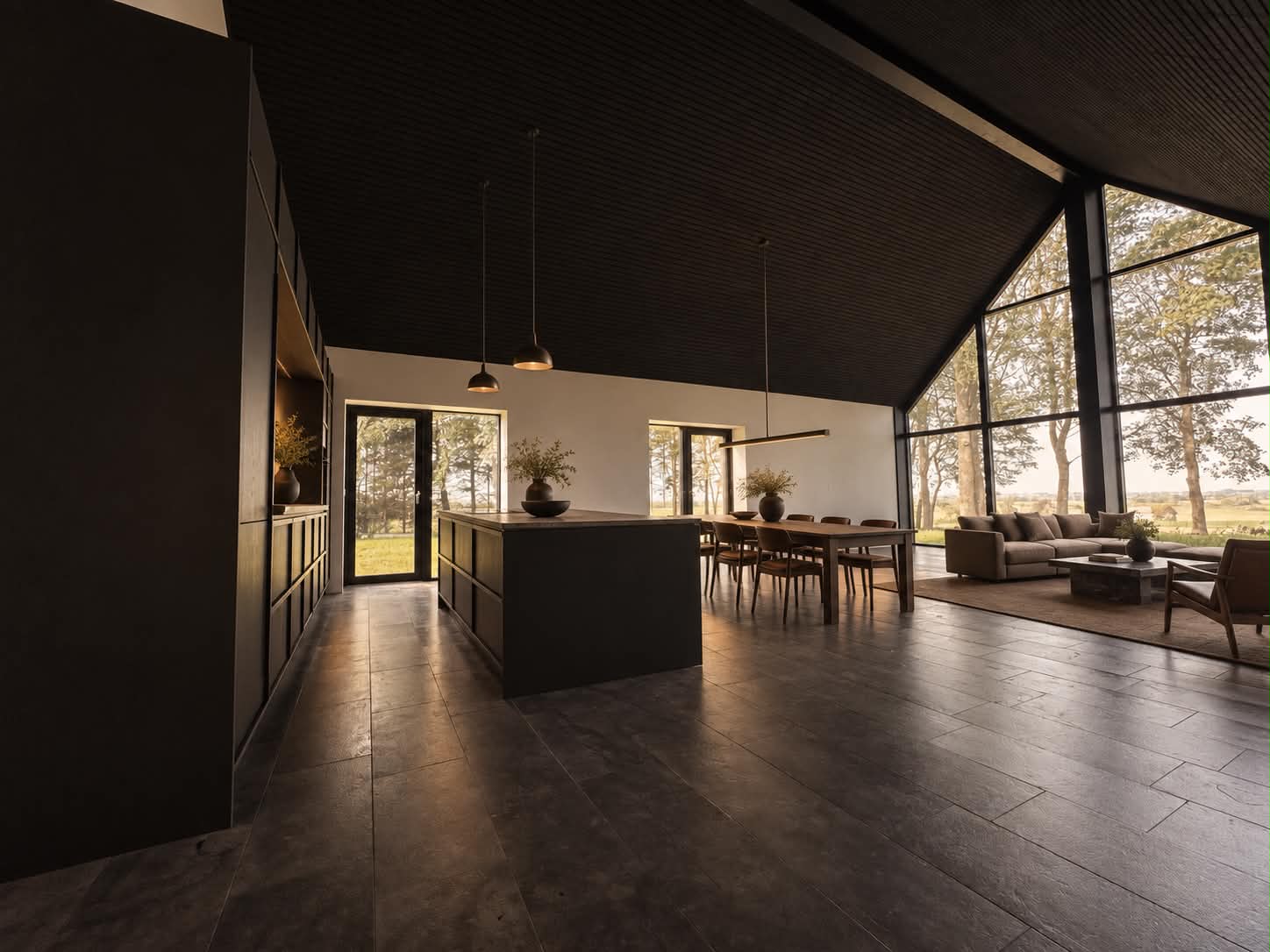 Køkken og opholdsrum med mørkt loft, store vinduespartier og udsigt til træerne.
